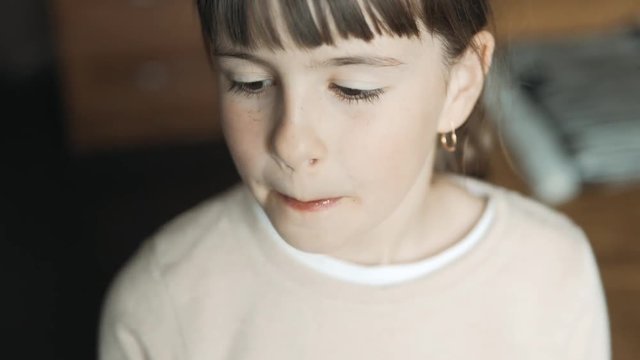 Portrait of teenager brunette girl eatsing big candy and smiling to camera, indoors shot