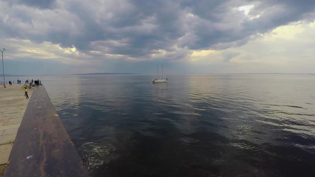 White two-masted yacht leaves the concrete pier under a cloudy sky and calm water