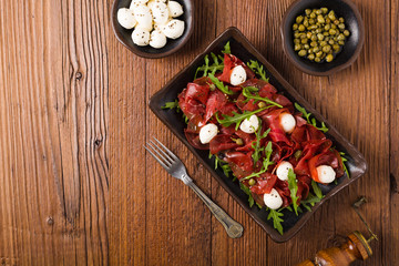 Beef carpaccio served with balls of mozzarella cheese, arugula and capers.