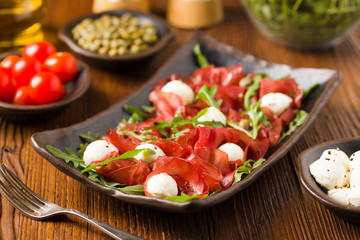 Beef carpaccio served with balls of mozzarella cheese, arugula and capers.