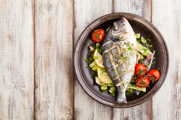 Baked whole fish, served with roasted vegetables and lemon.
