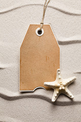 Blank paper label and starfish on beach sand