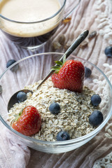Breakfast: glass bowl with flakes and berries, cup of black coffee on the pink tissue