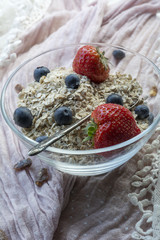 Glass bowl with cereals, strawberries and blueberries on the pink tissue