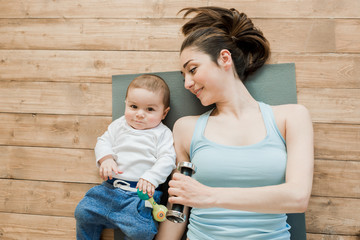 Top view of mother with baby boy lying on floor and playing with dumbbells