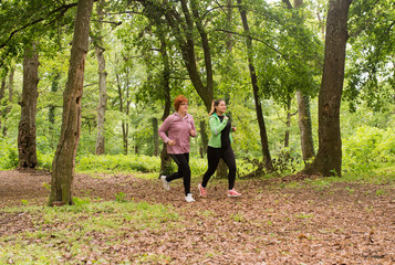 Mother and daughter wearing sportswear and running in forest at mountain