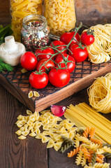 Assortment of raw types and shapes of italian pasta and wooden board on a black slate background. Close up. Top view and copy space.