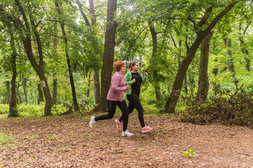 Mother and daughter wearing sportswear and running in forest at mountain