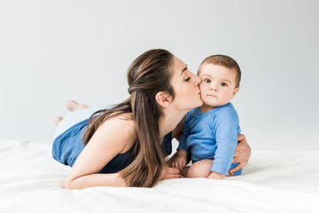 Portrait of mother kissing her adorable child while lying on bed