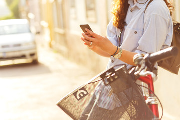 Close up of beautiful young woman siting on bicycle in old town and looking at mobile phone.