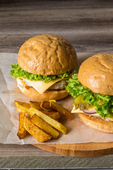 Home made hamburger with chicken, onion, cucumber, lettuce and cheese on wooden table with potato fries