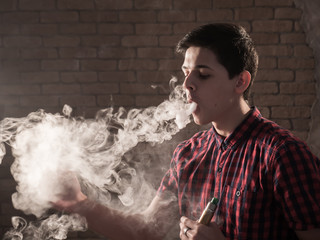 Obraz na płótnie Canvas Young man stands in profile and breathes out a solid smoke stream in studio