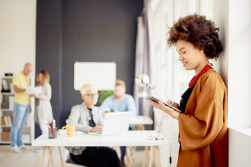 African american businesswoman standing in modern office and using tablet device. Beside her colleagues