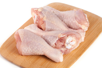 four raw chicken drumsticks on a wooden cutting boardn white background