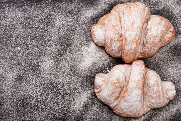 two croissant sprinkled with powdered sugar on black stone background with copy space for your text. Top view