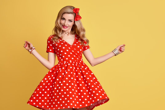 Fashion Woman Smiling in Red Polka Dots Summer Dress. PinUp Sensual Blond Girl Having fun. Trendy Stylish Curly hairstyle, Makeup, red Bow. Glamour Playful Sexy Beauty pinup Model. Vintage on Yellow