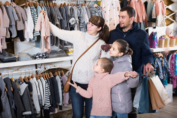 family with daughters showing their purchases in children’s clothes shop