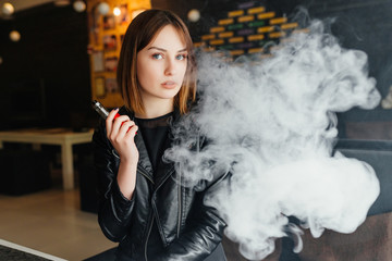 Vaping. Young beautiful girl smoking ( vaping ) e-cigarette with smoke in restaurant. Vapor concept.