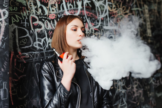 Beautiful young woman inhaling smoke. young girl vaping against the background of a painted wall