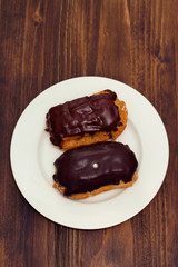 chocolated eclairs on white dish on wooden background