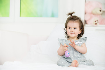 Sweet happy little baby girl sitting on bed, looking away.Shallow doff.Copy space