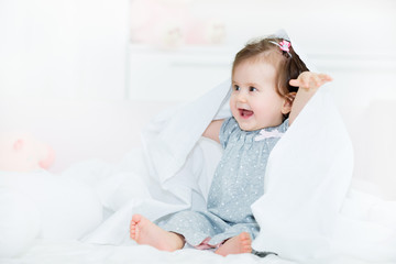 Baby little girl laughing for a joy while playing with a bed sheet.Shallow doff, copy space