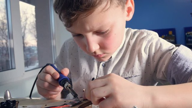 Concentrated boy soldering copter parts. Close-up. 4K.