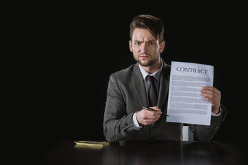 portrait of serious businessman pointing on contract isolated on black