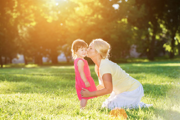 Fototapeta premium Mom kissing her little girl in the sunset park.Lens flare