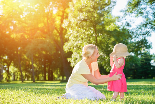 Mom And Little Girl Playing Peek A Boo With A Big Hat In The Sunset Park.Lens Flare, Copy Space