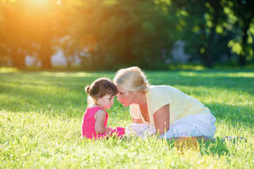 Mom and little girl softly whispering face to face in the sunset park.Lens flare