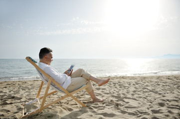 Man relaxing with tablet on the beach sitting on a deckchair