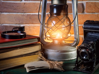 Still life kerosene lamp shines on  wooden desktop  stone brick background book camera.