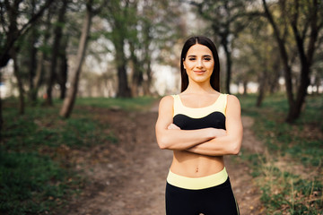 Beautiful fitness girl with crossed hands posing in the park after training