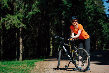 Obraz premium Young pretty woman in helmet and sunglasses standing with bicycle on the forest road. Healthy lifestyle concept. Girl with bike.