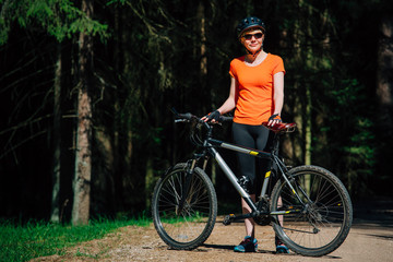 Fototapeta na wymiar Young pretty woman in helmet and sunglasses standing with bicycle on the forest road. Healthy lifestyle concept. Girl with bike.