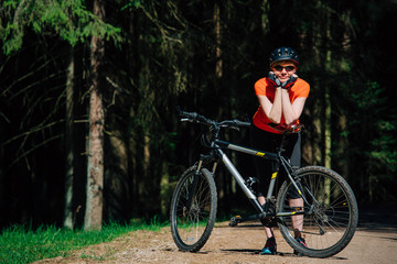 Obraz premium Young pretty woman in helmet and sunglasses standing with bicycle on the forest road. Healthy lifestyle concept. Girl with bike.
