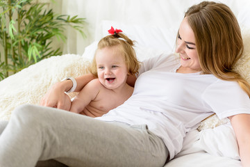 Joyful infant relaxing with her mom on bedding