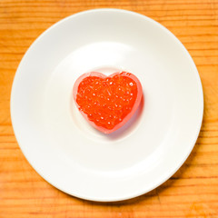 Closeup on love heart shape red caviar delicacy on white plate, closeup light macro background