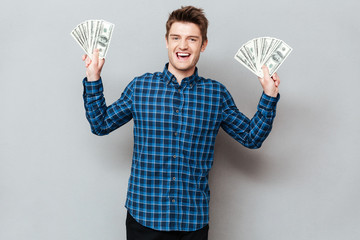 Cheerful man standing over grey wall holding money.