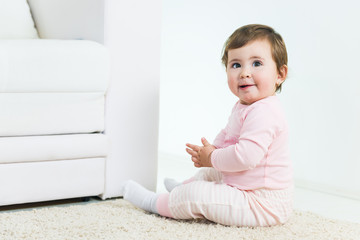 Sweet baby little girl sitting on floor next to the sofa , looking at camera.Copy space, shallow doff