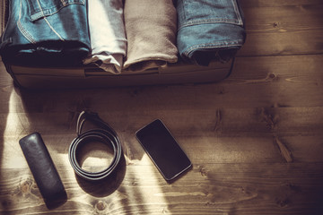 Open suitcase with male clothes for trip on the wooden floor. Toned image.