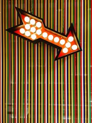 Luminous arrow. A lit-up luminous orange arrow pointing on the lower right over a multicolored plastic background.