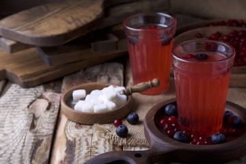 Two glasses with red drink, berries, sugar on wooden brown surface opposite the red brick wall with copy space. Still life. Rustic style kitchen