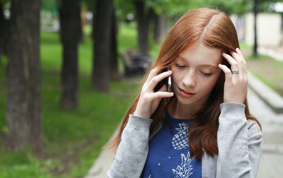 Beautiful young girl talking on a phone in city park.