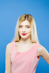 Young Woman with Long Blond Hair and Professional Makeup on Blue Background. Portrait of Cute Girl in Studio.