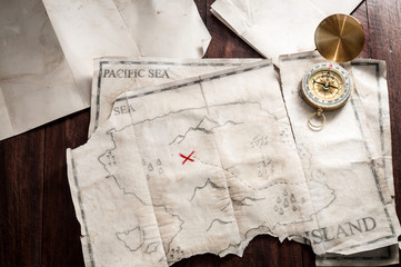 Table with vintage papers and old crumpled and folded map of fake Island with treasure chest.