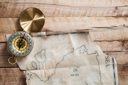 Top view to gold compass on wooden desk with fake handmade broken vintage map