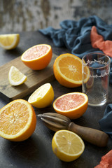 Halves and slices of citrus fruits on wooden board and wooden juicer on dark concrete surface. process of making juice