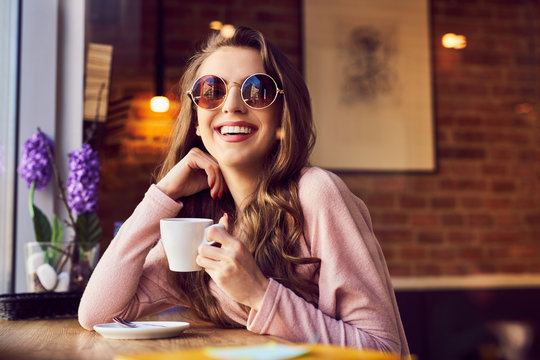 Smiling woman with sunglasses enjoying coffee at cafe